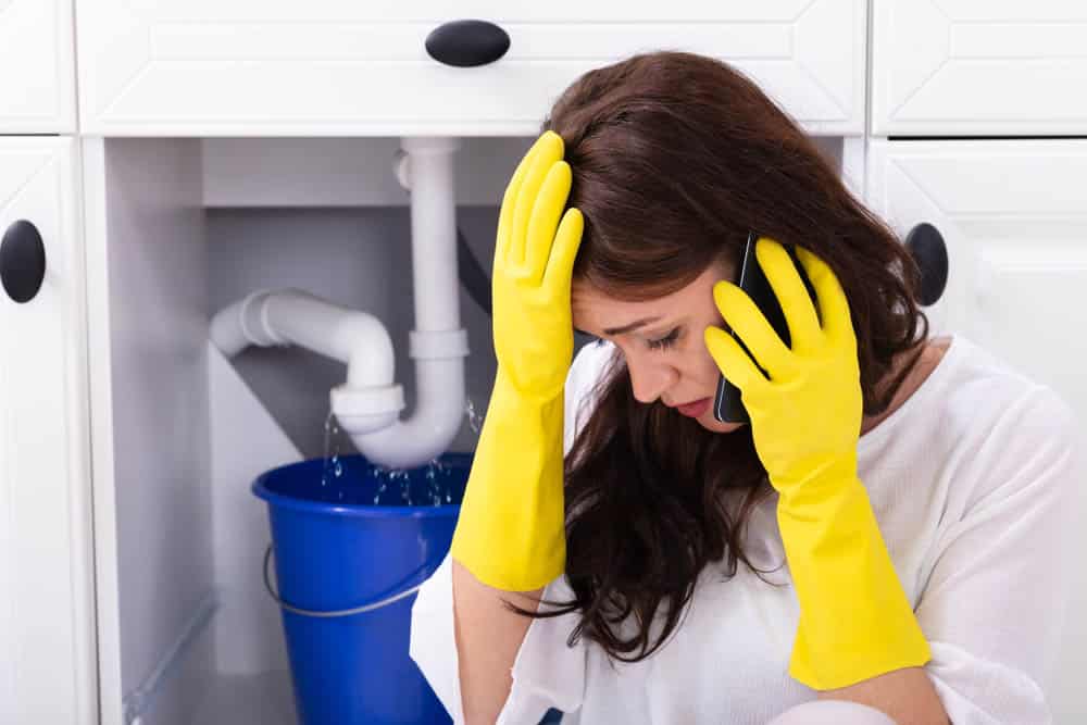 woman calling a plumber Acworth, GA in front of leaking sink pipe