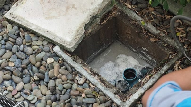 Plumber repairing clogged grease trap with auger machine.